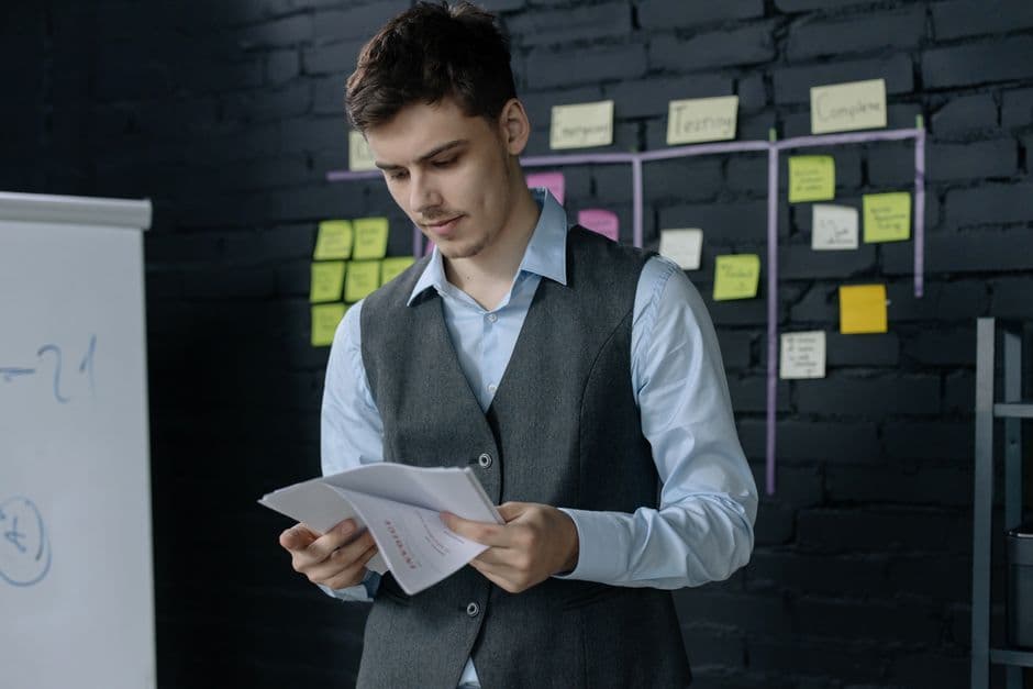 A young man reviewing documents in an office with a black brick wall and sticky notes background.