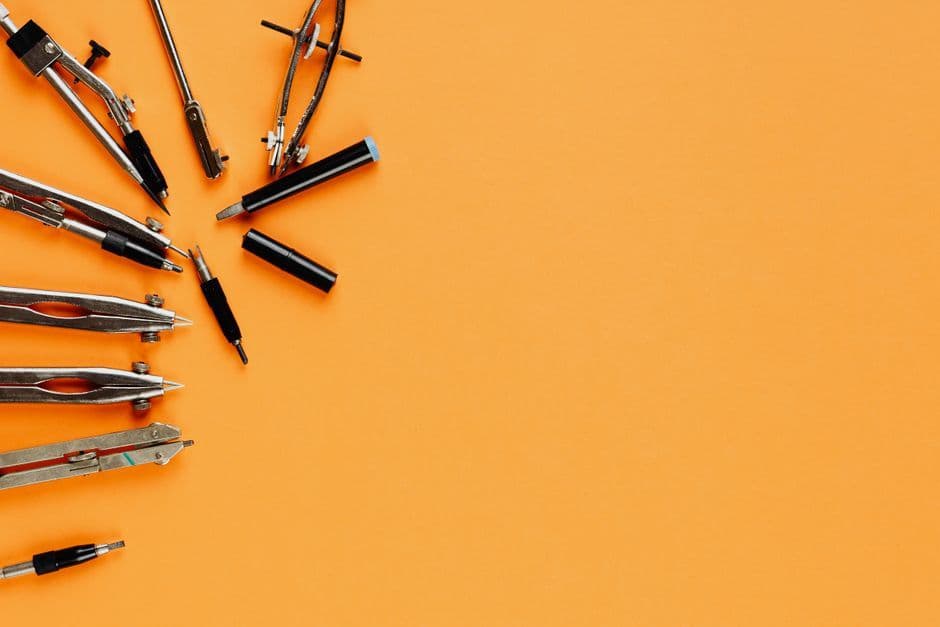 Top view of various drawing tools and compasses on an orange background with copy space.