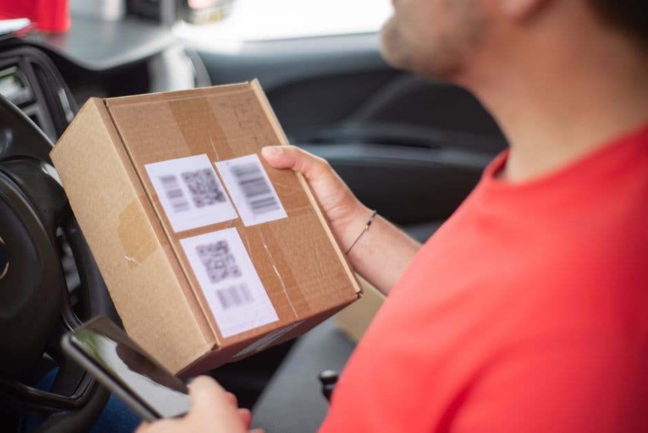 Close-up of a person holding a package with QR codes inside a car, emphasizing delivery and technology.